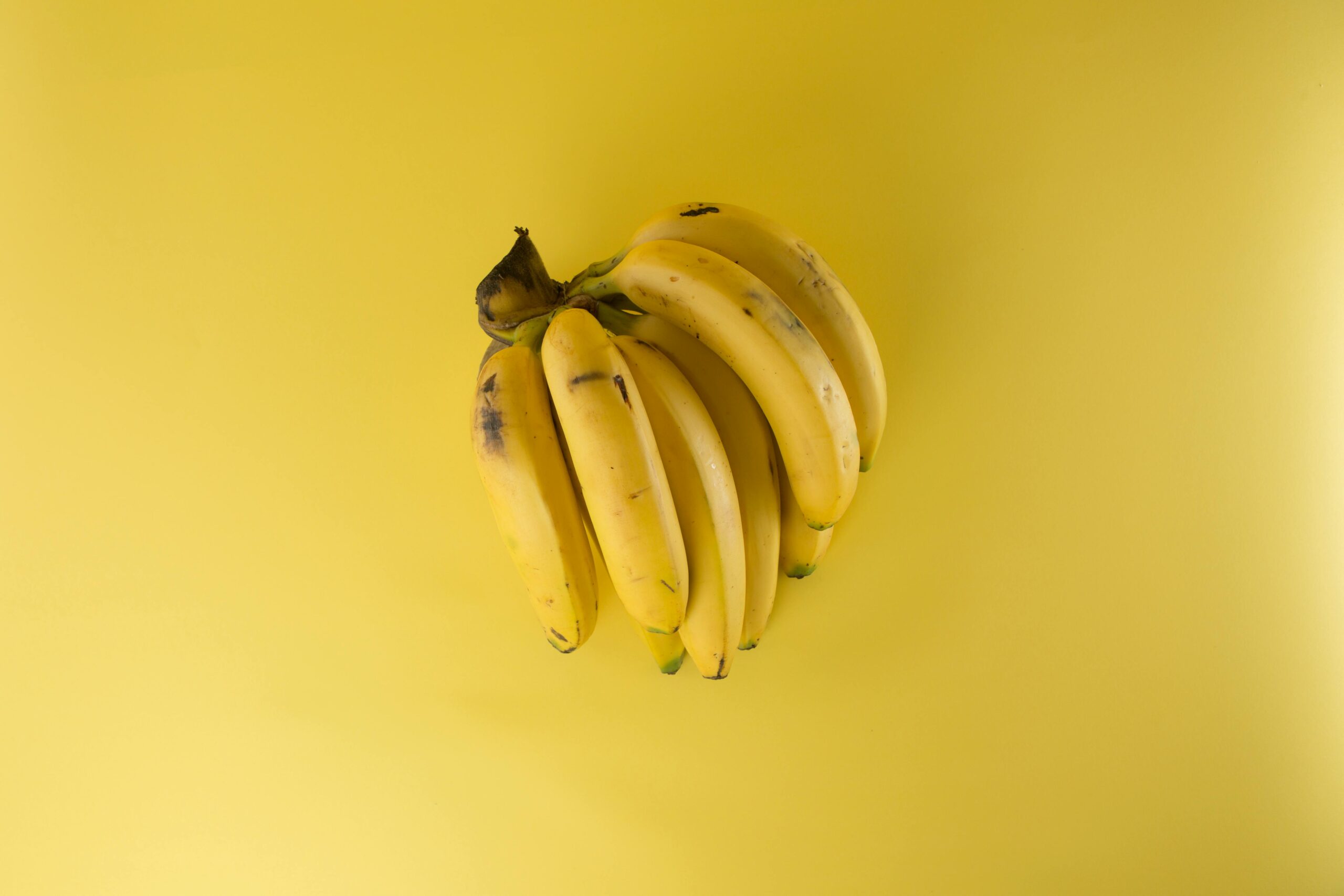 A vibrant bunch of ripe bananas on a matching yellow background, evoking freshness.